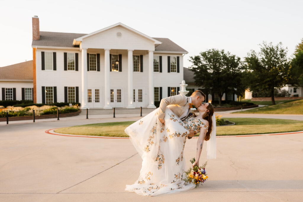 the groom dips his brides in the front drive with the milestone mansion beaming in the background. captured by wedding photographer shelly voss.