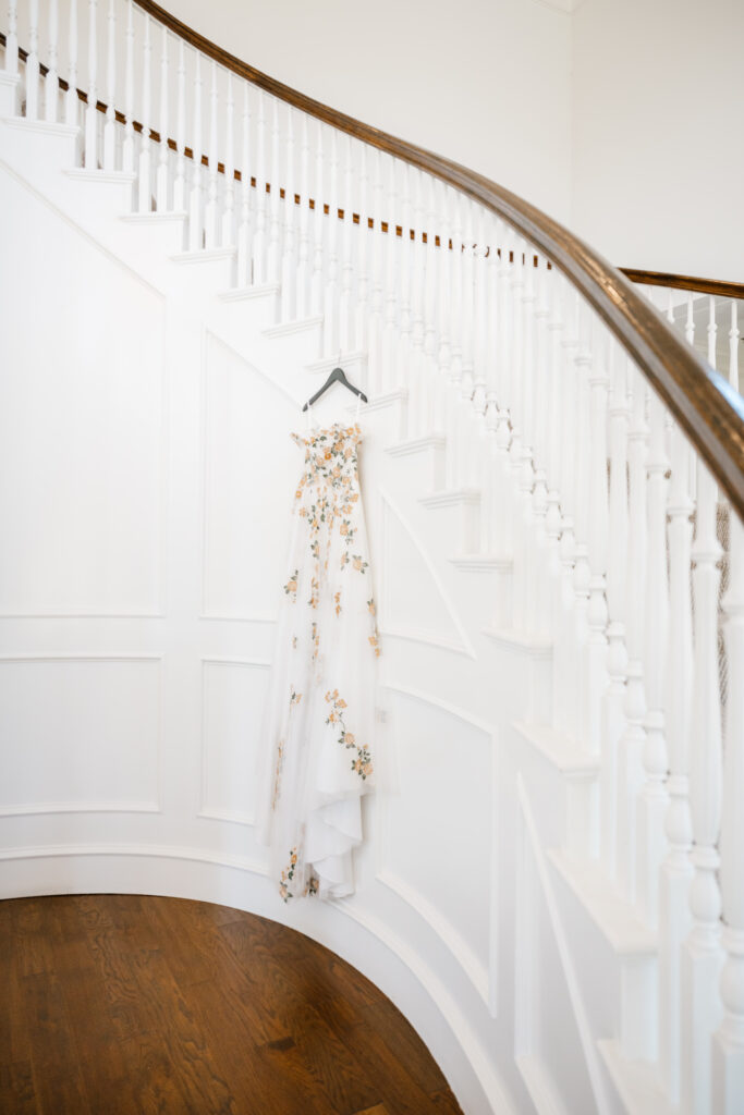 a picture of a floral wedding dress hanging from the spiral staircase at the milestone mansion in denton, texas