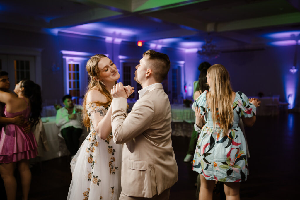 bride and groom dance with hands clasped smiling at each other at their wedding recpetion held at the milestone denton, texas