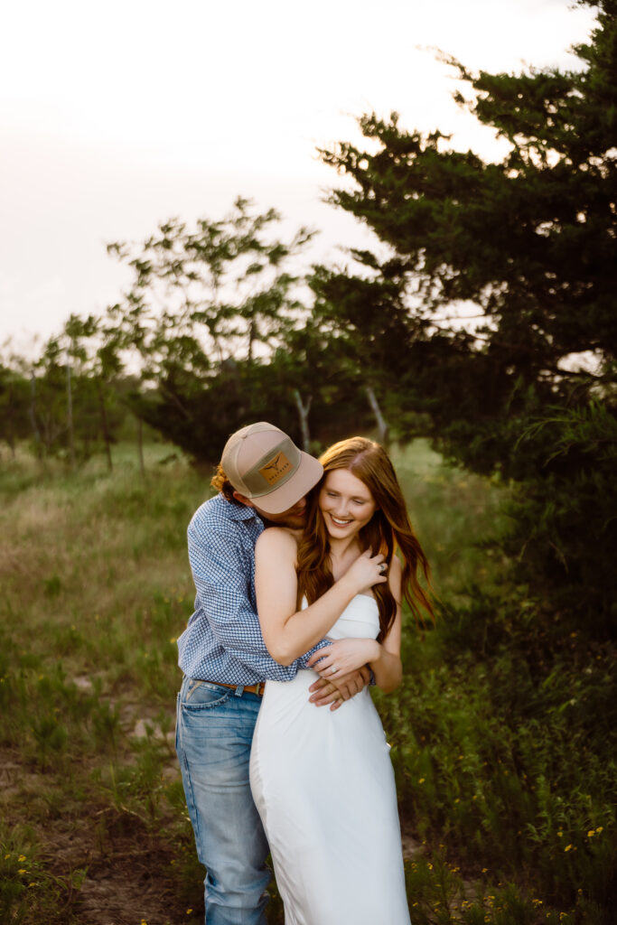 a groom hugs his fiancé from behind while laughing. Shelly Voss photography captures their sweet moment