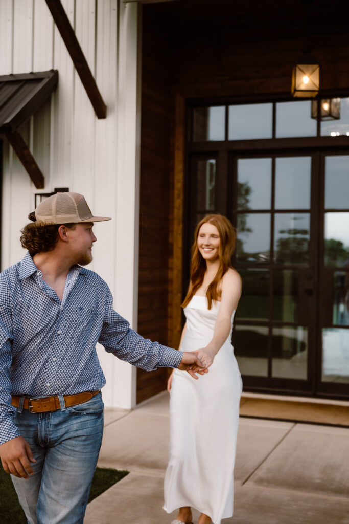 a couple stands out front of Davis and grey farms walking hand in hand while smiling.