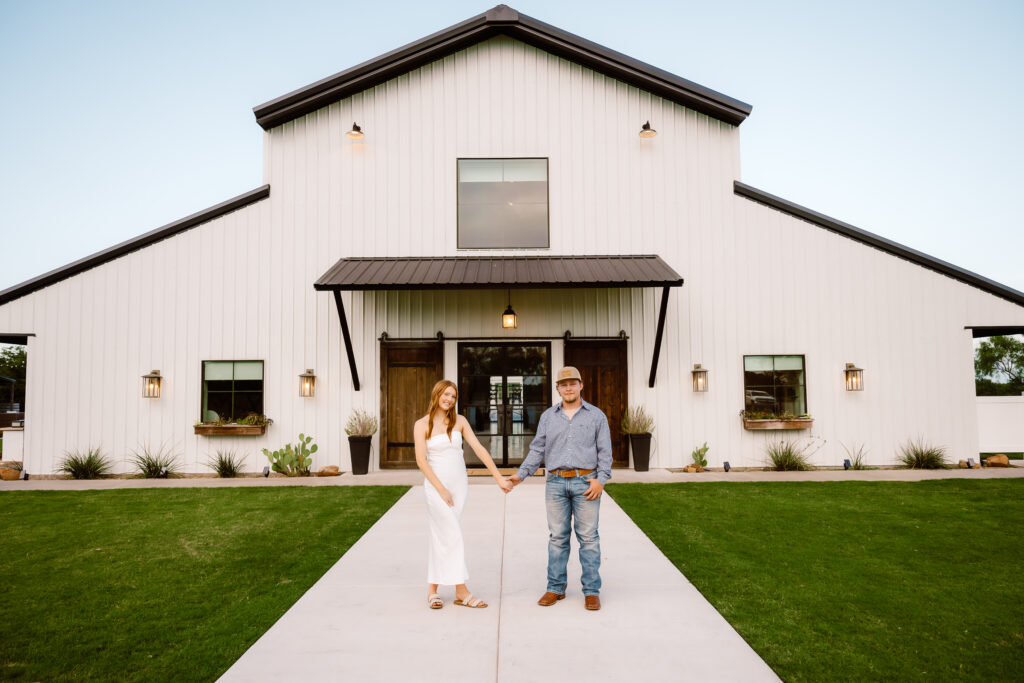 Picture of a couple holding hands standing in front of Davis and Grey Farms in Celeste Texas while Shelly Voss captures the photo during blue hour.