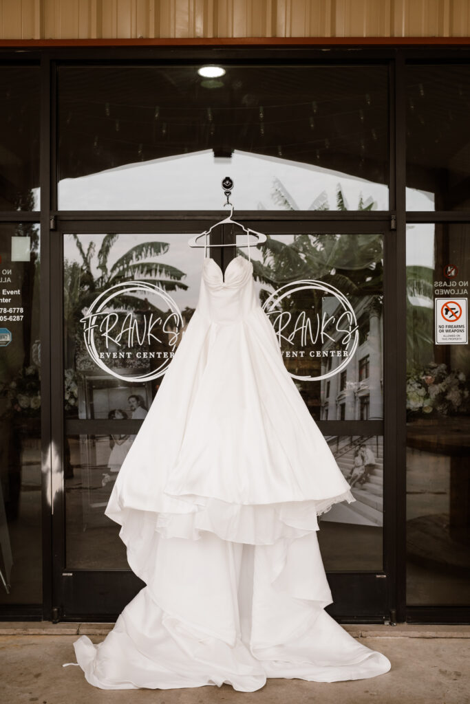 The brides large wedding gown hangs at the entrance of the venue while Shelly Voss photographs it
