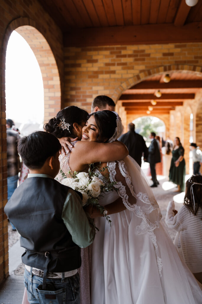 the brides shares a hug with her mom after exiting the Catholic Church following her ceremony while Shelly Voss photography takes the candid photo
