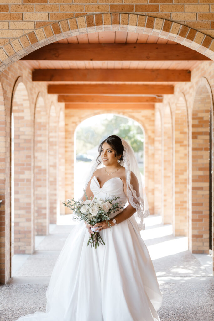 a bride stands with her bouquet in hand under the arch at the Catholic Church while Shelly Voss captures the moment.
