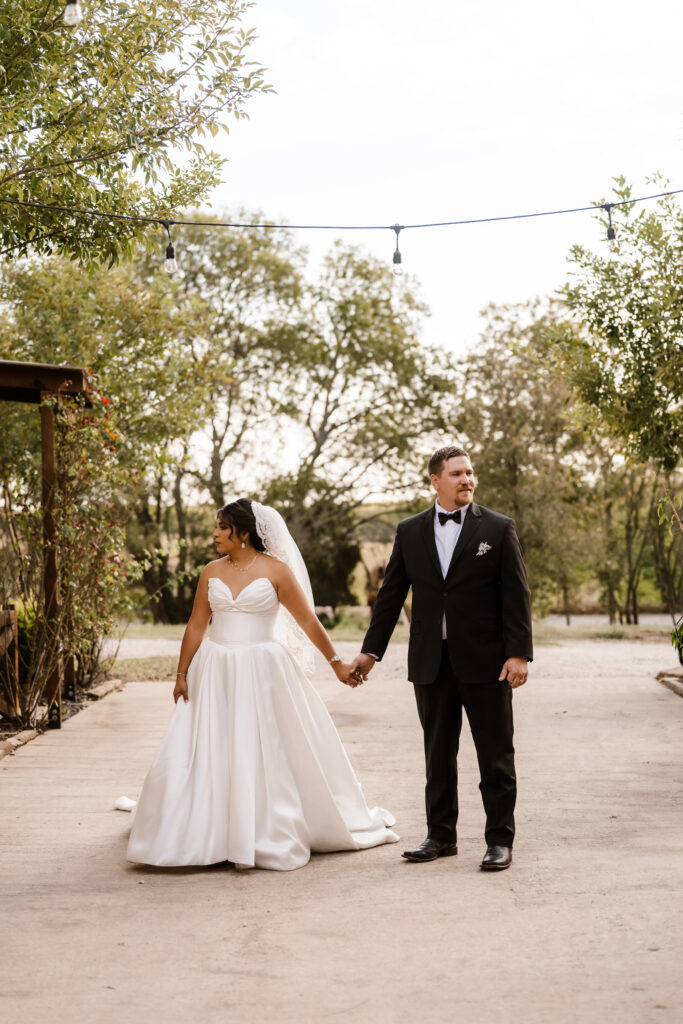 the bride and groom stand hand and hand looking opposite directions as Shelly Voss captures the moment.