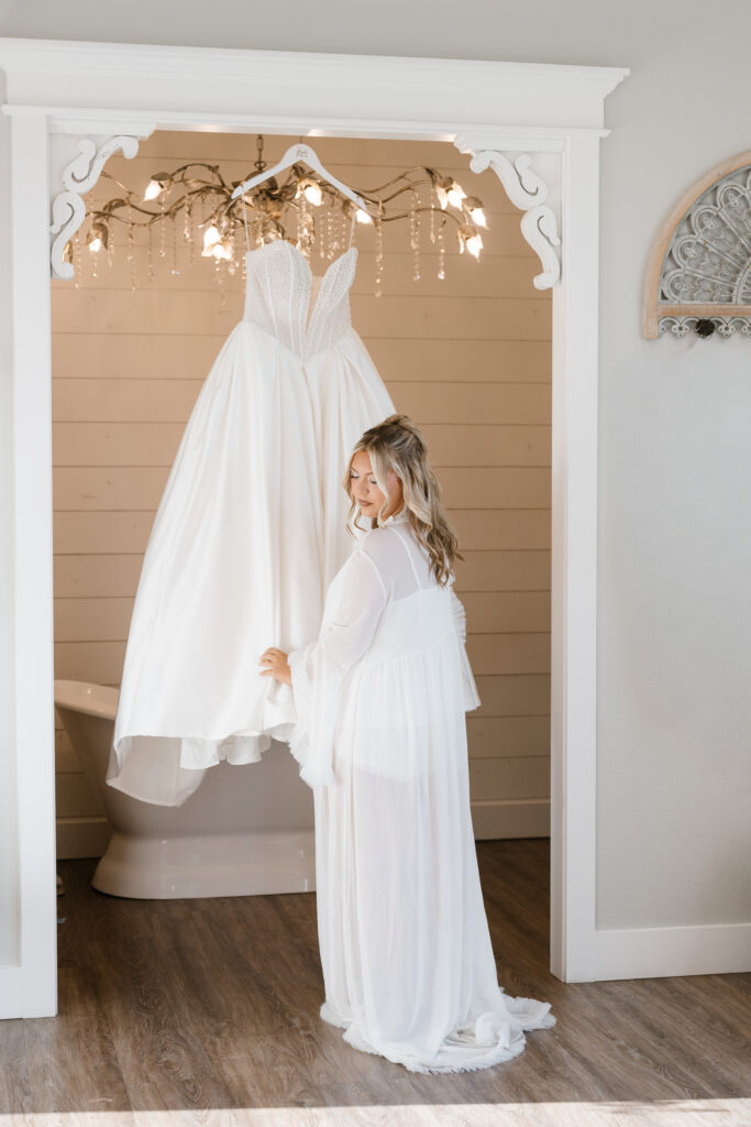 Bride standing in front of wedding dress in Chandelier Farm bridal suite
