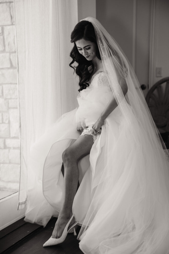 bride slides her garter up her leg while shelly voss photography captures the moment.

