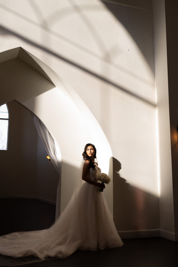 a bride stands in the light coming through the arched windows at the castle wedding venue in rockwall, texas captured by shelly voss photography. 
