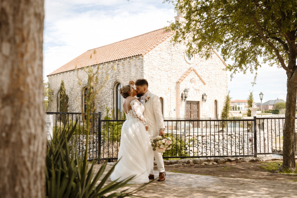 Romantic bride and groom portraits outside Bella Donna Chapel with Adriatica stone architecture backdrop while bride and groom share a kiss