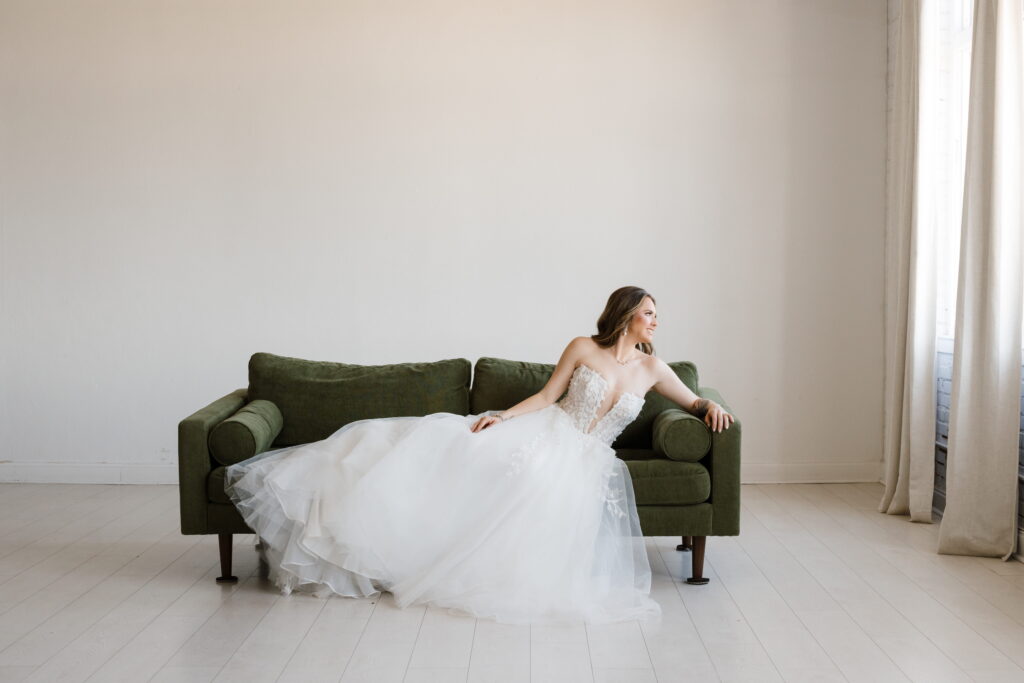 bride poses editorial style on green sofe during her bridal session with shelly voss